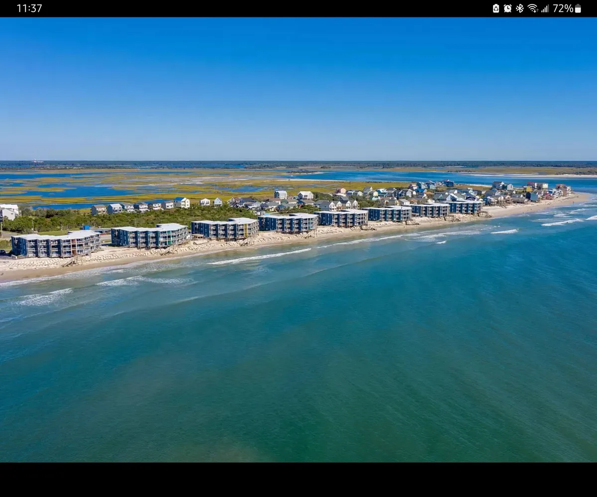 A panoramic view of beachfront properties overlooking shimmering ocean waves, with a blend of green marshland and blue sky. The scene hints at a variety of activities—beach walks, water sports, and family gatherings—while showcasing the proximity of the condos to the shoreline.