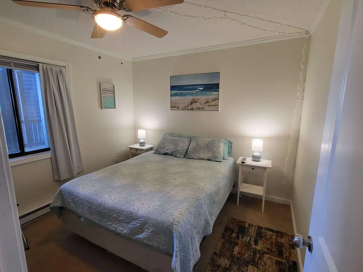 A peaceful bedroom scene featuring a neatly made bed, wall art above the headboard, matching side tables with lamps, and a window letting in natural light. The overall atmosphere is tranquil and welcoming, perfect for restful sleep.