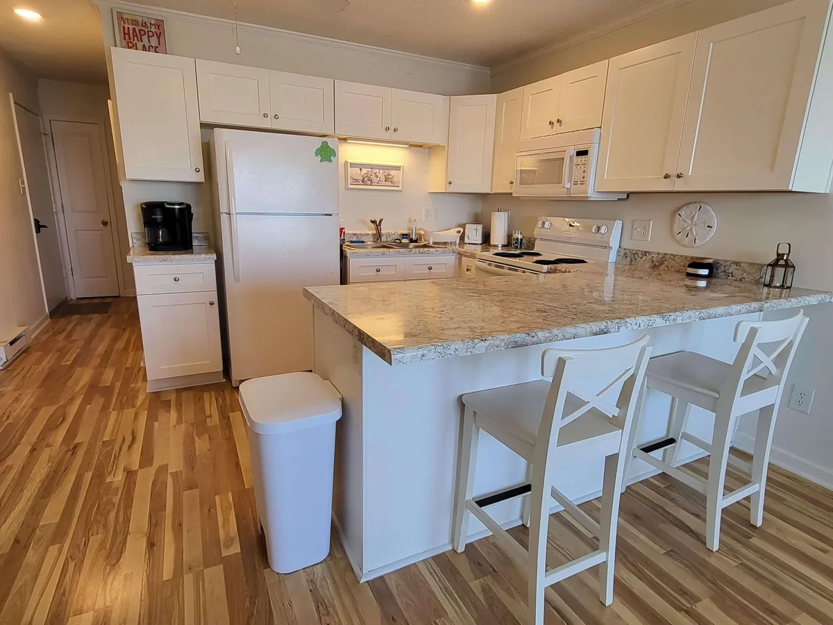 This image showcases a stylish kitchen with granite countertops, white cabinetry, modern kitchen appliances, and bar stools. The setting is inviting, well-lit, and designed for both cooking and socializing.